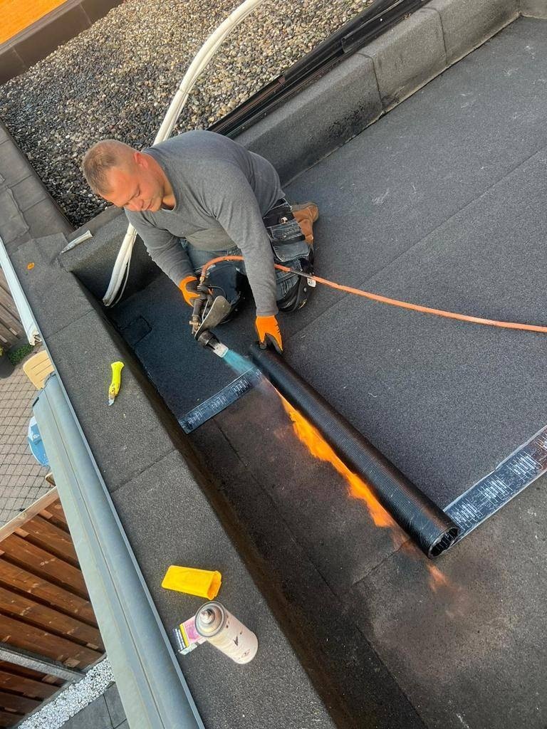 Een dakdekker brandt een bitumen baan vast op een plat dak